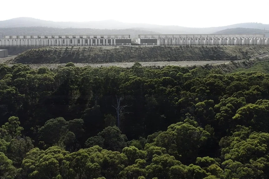 A computer render of a long, low beige coloured building among trees