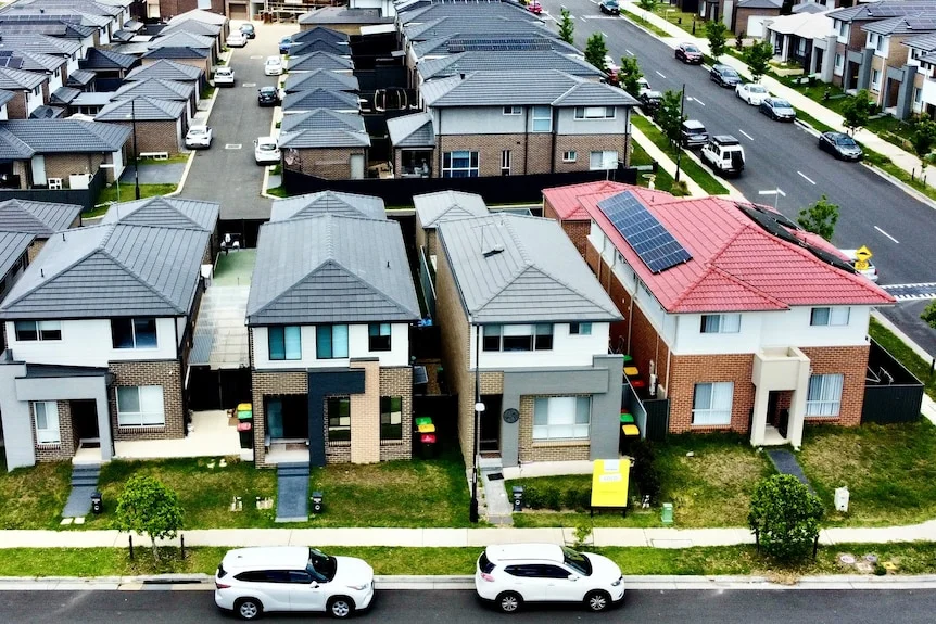 Aerial shot of dozens of houses in neat rows in a new outer-suburban housing estate.