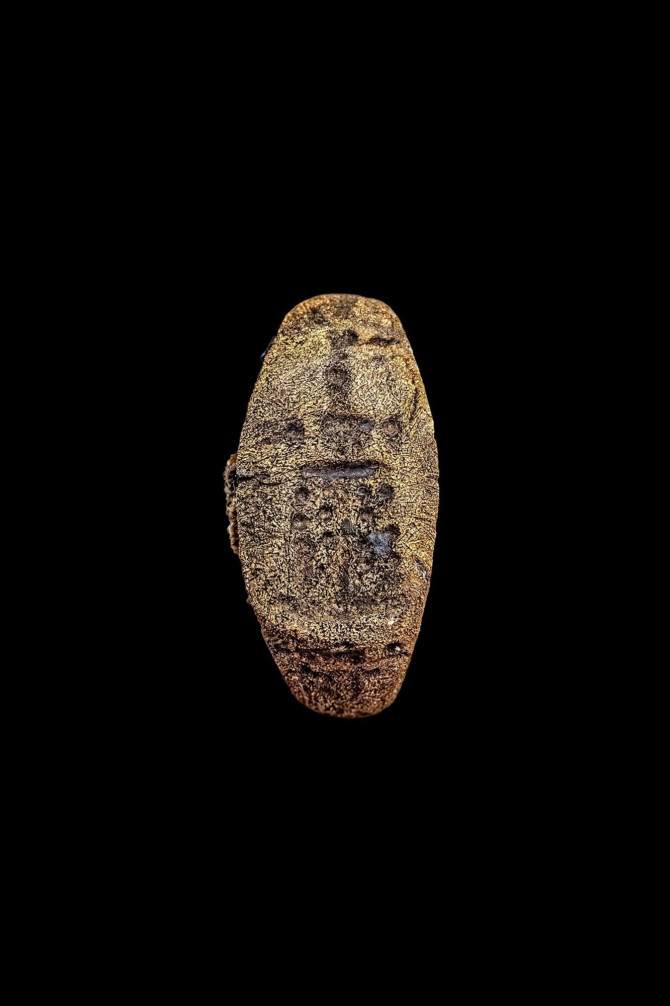 A close up of a bronze ring with engravings on it against a black background.